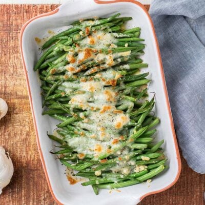 A white dish with baked garlic green beans topped with browned mozzarella cheese.