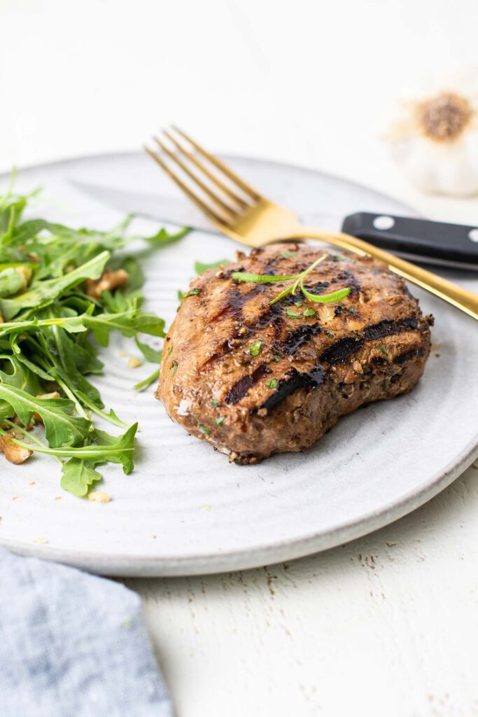 A grilled pork chop on a plate with an arugula salad.