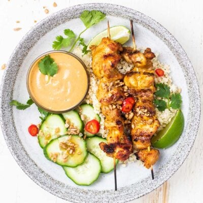 A plate showing 2 chicken satay skewers with cauliflower rice and lime.