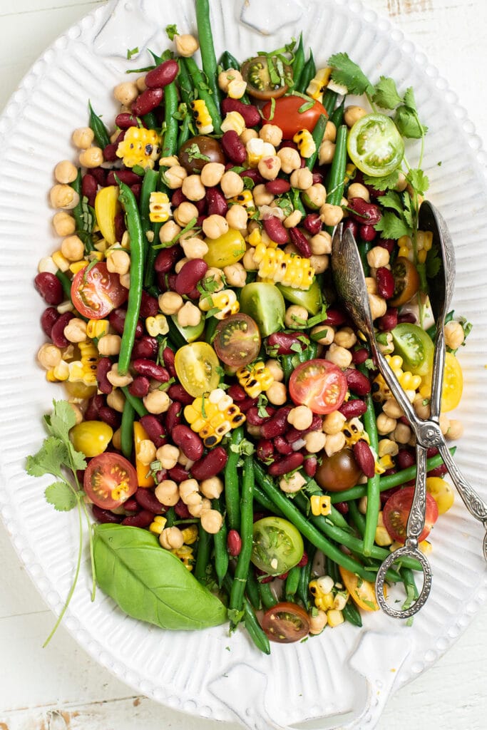 A large white platter with a 3 bean salad garnished with basil leaves.