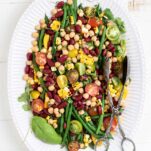 A colorful 3 bean salad on a platter with tomatoes, basil, and grilled corn.