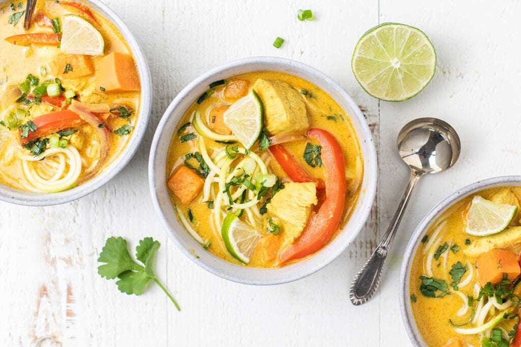 Three bowls of zoodle soup shown with soup spoons.