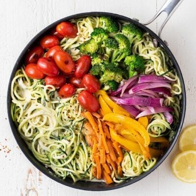 A skillet with zoodles tossed in a creamy lemon sauce topped with colorful veggies.