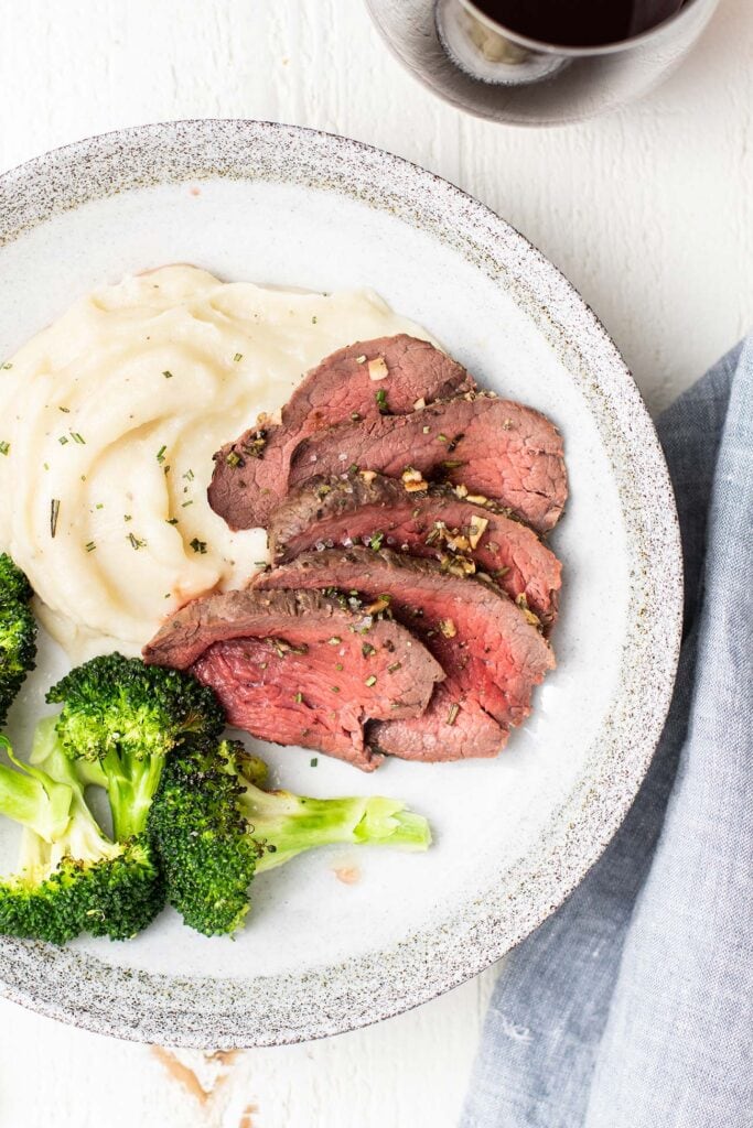 A plate with mashed potatoes, broccoli, and with thin slices of this beef tenderloin recipe..