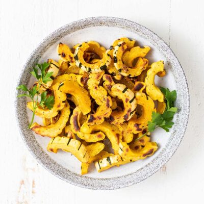 A bowl filled with delicata squash garnished with parsley.