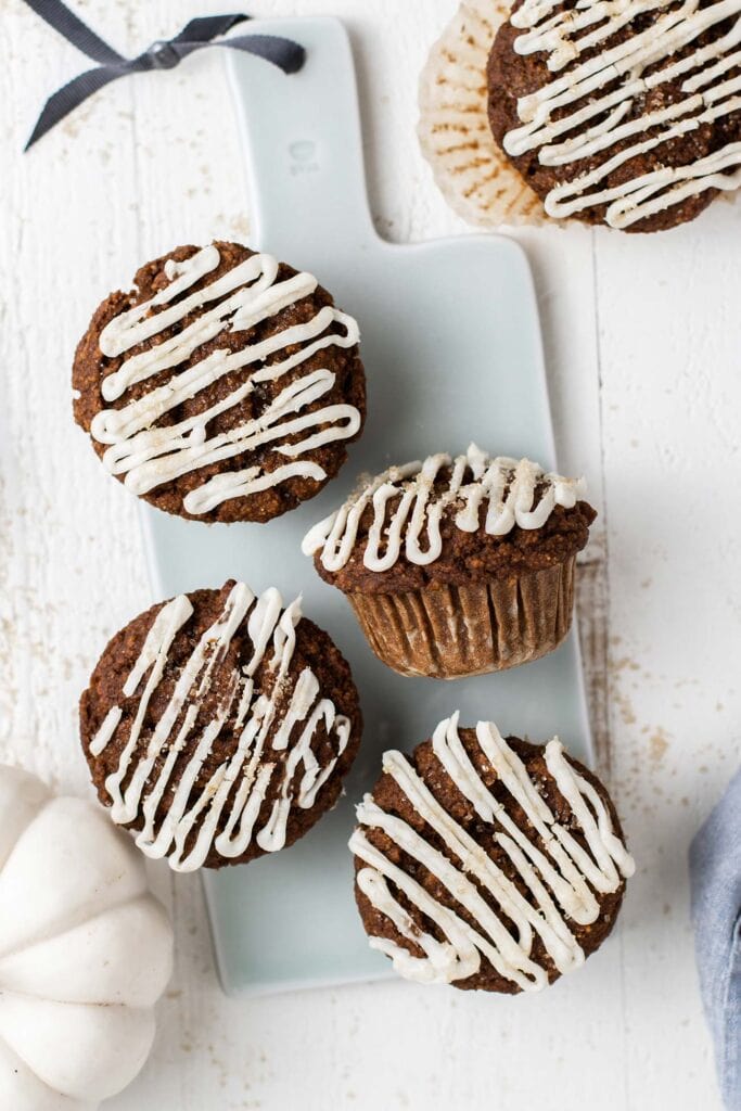 Pumpkin gingerbread muffins on a blue cutting board drizzled with cream cheese glaze.