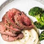 A close up photo of a plate with potatoes, broccoli, and thinly sliced beef tenderloin.