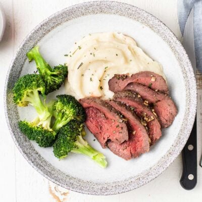 Slices of medium rare chateaubriand, on a plate with potatoes and broccoli.