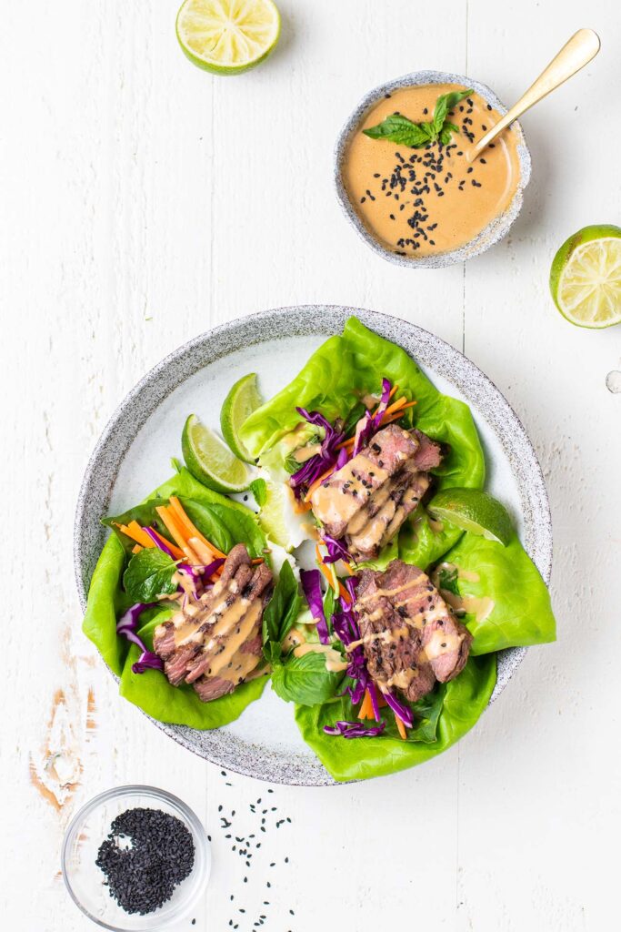 A plate with 3 large lettuce leaves filled with thinly sliced steak.