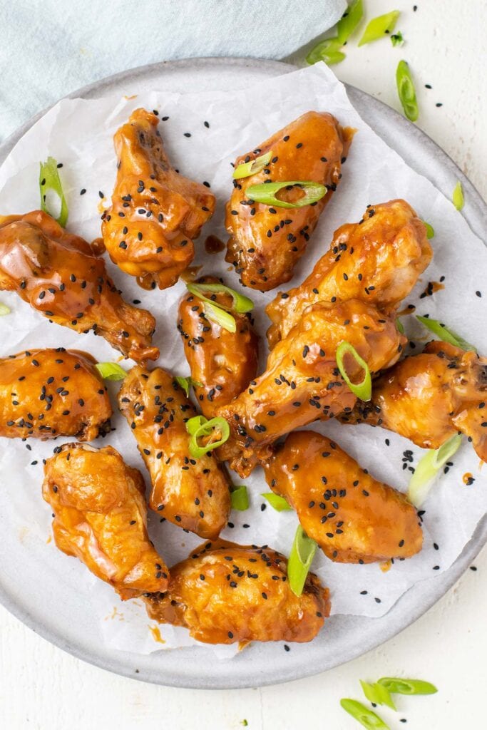 Chicken wings shown tossed in a thick Asian sauce garnished with black sesame seeds and green onions.
