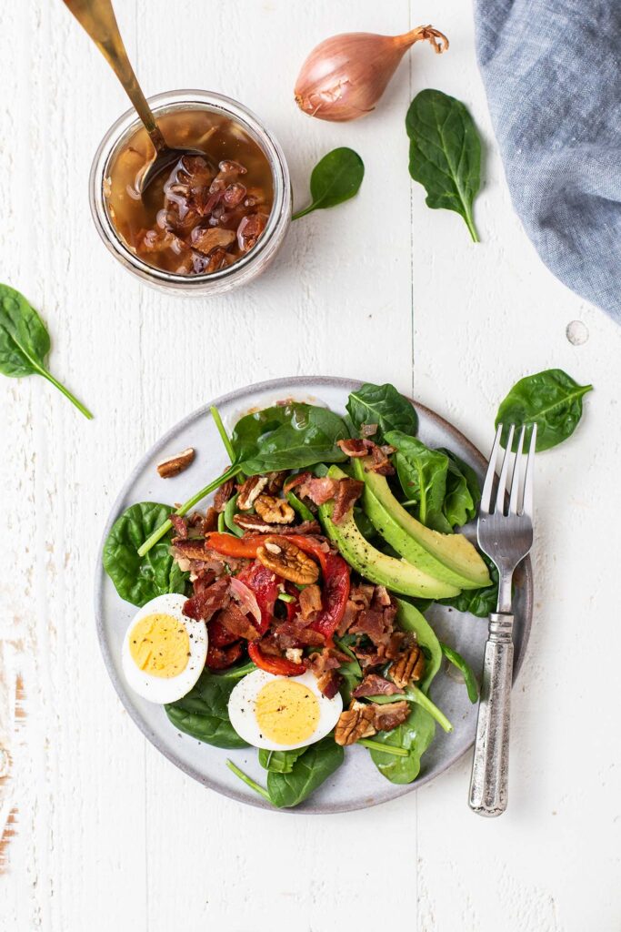 A gray plate with a wilted spinach salad, next to a jar of hot bacon dressing.