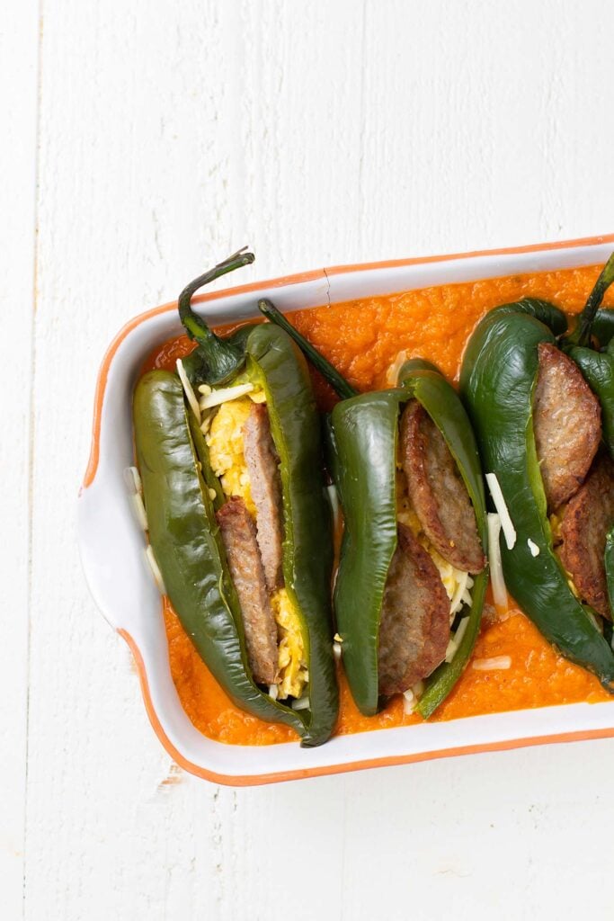 Chiles stuffed with sausage and egg siting in a casserole dish with a red relleno sauce.