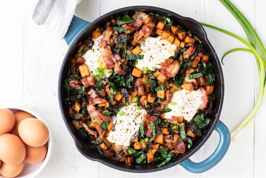A sweet potato breakfast skillet baked with 4 eggs on top, shown next to a bowl of whole eggs.