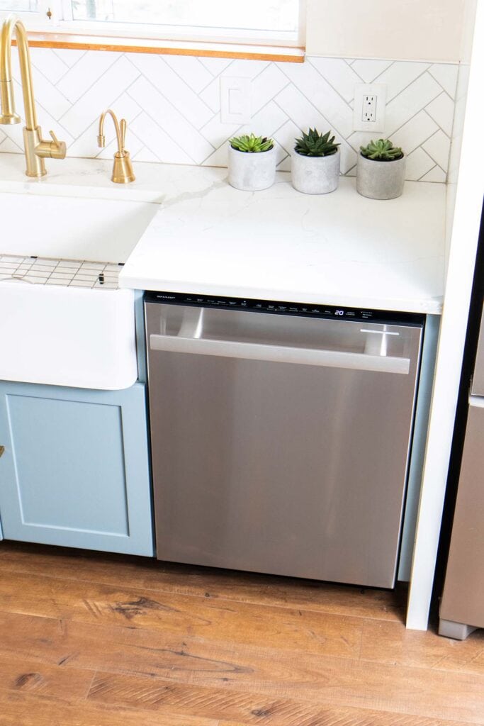 A view of a dishwasher installed next to a white farmhouse sink.