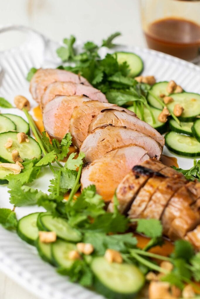 A view of a sliced pork tenderloin garnished with cucumbers and cilantro.