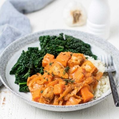 A plate with cauliflower rice, sauteed kale, and topped with African Chicken Stew.