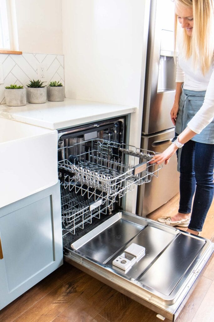 A woman pulling the top rack of an empty dishwasher out of an open machine.