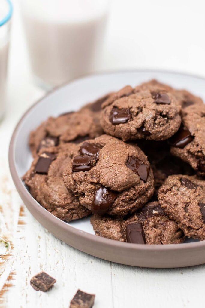 A plate with a stack of double chocolate chip cookies shown with melty chocolate chunks.