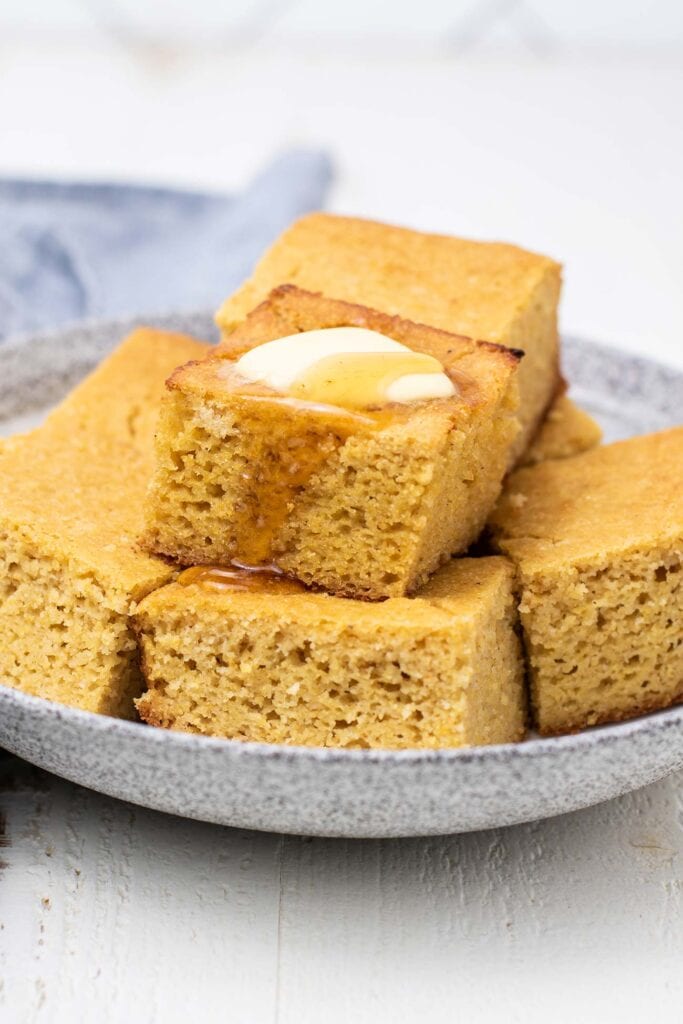 Cornbread slices stacked up, and with butter and honey dripping off the top.