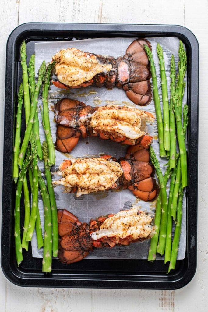 Lobster tails on a baking tray with asparagus.