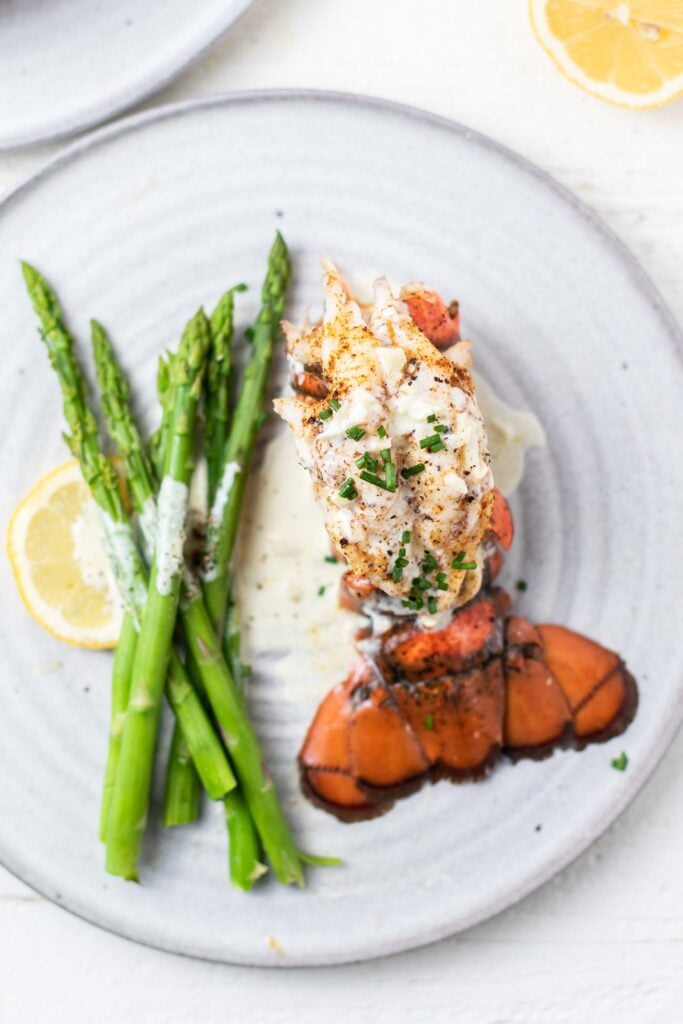 A lobster tail drizzled with cream sauce on a plate with asparagus.