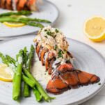 A lobster tail drizzled with cream sauce on a plate with asparagus.