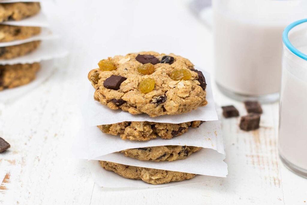 A stack of gluten free oatmeal raisin cookies in front of two glasses of milk.