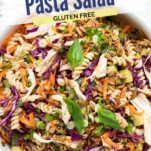 A close up look at a bowl of pasta salad with carrots, purple cabbage, chicken and herbs.