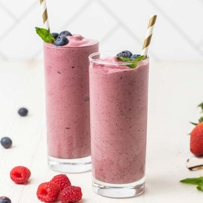 Two glasses filled with an acai smoothie garnished with mint and berries.