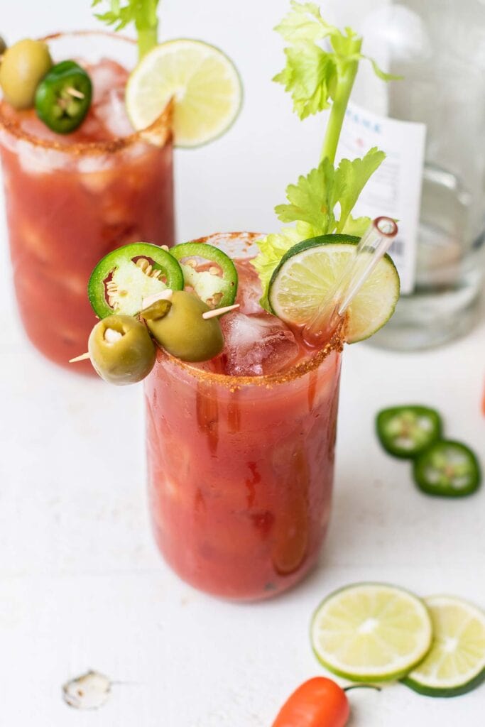 Two bloody maria cocktails garnished with celery, olives, and jalapeno.