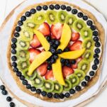 A whole fruit pizza shown on a pizza stone.