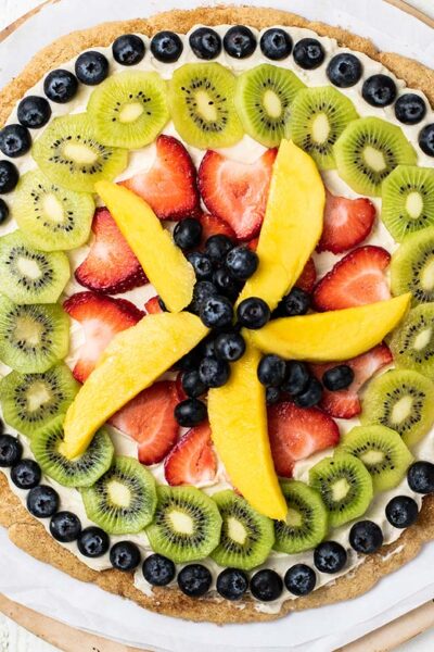 A whole fruit pizza shown on a pizza stone.