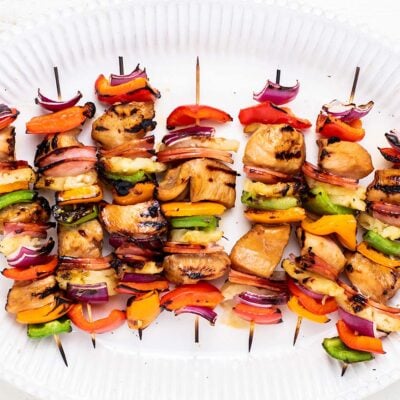 A white platter with colorful grilled teriyaki chicken skewers.