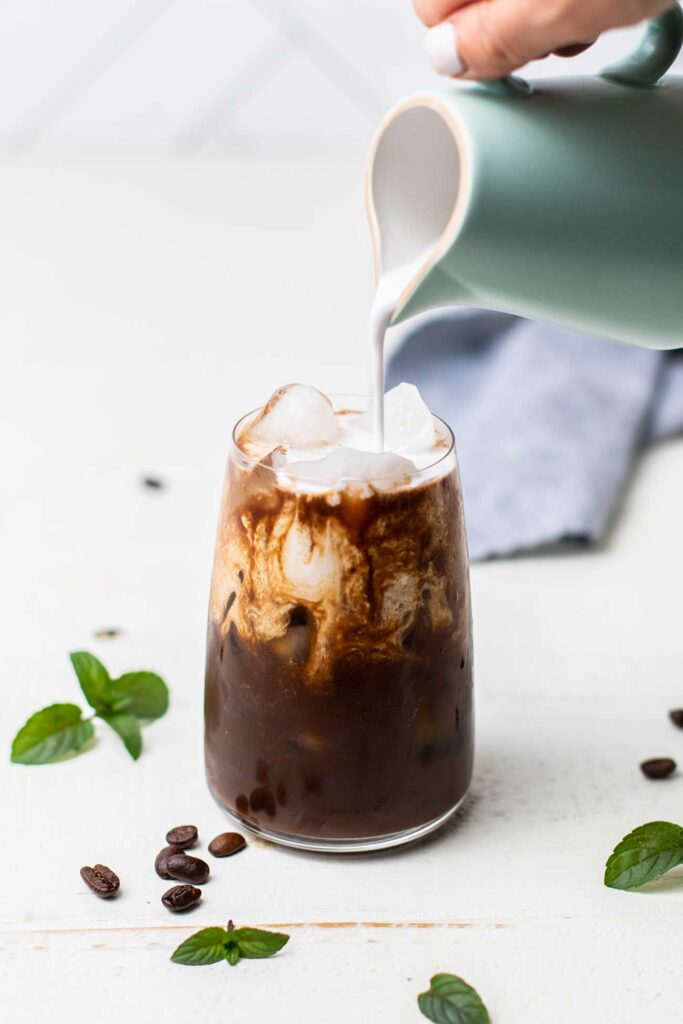 Coconut milk being poured into an iced mocha latte.