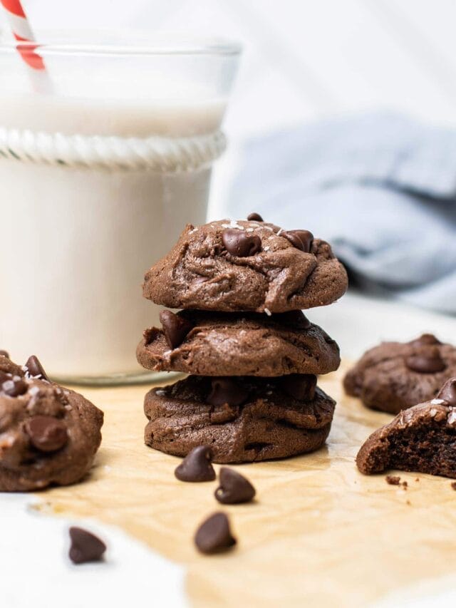 A stack of 3 flourless chocolate cookies in front of a glass of almond milk.