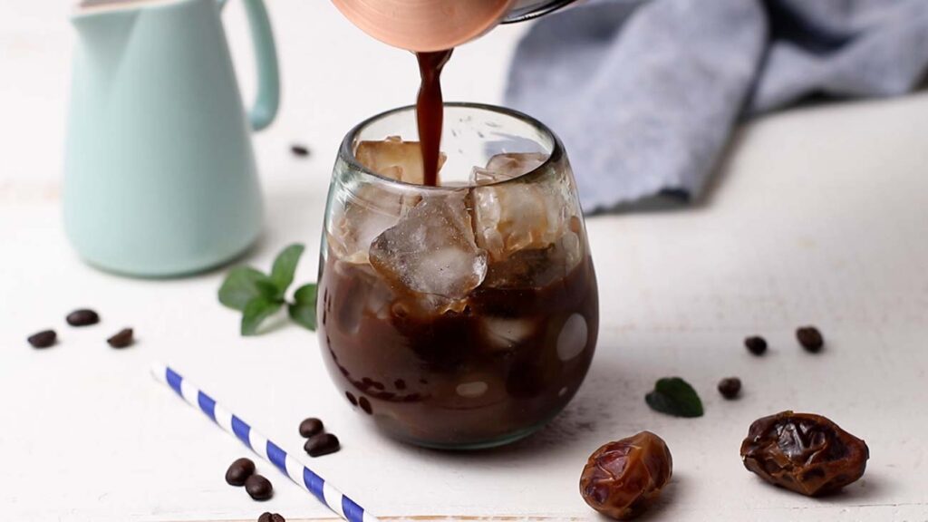 A glass of ice with coffee concentrate being poured over the top.