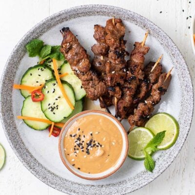 A plate with beef satay skewers and satay dipping sauce, garnished with lime and mint leaves.