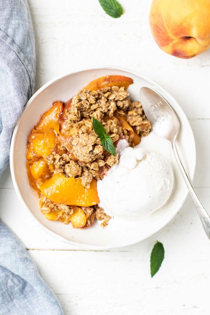 A top down view of a bowl of peach crisp served with vanilla ice cream.