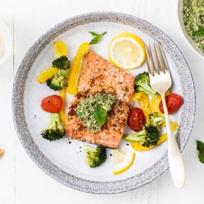 A plate with a piece of pesto salmon surrounded by colorful roasted veggies.