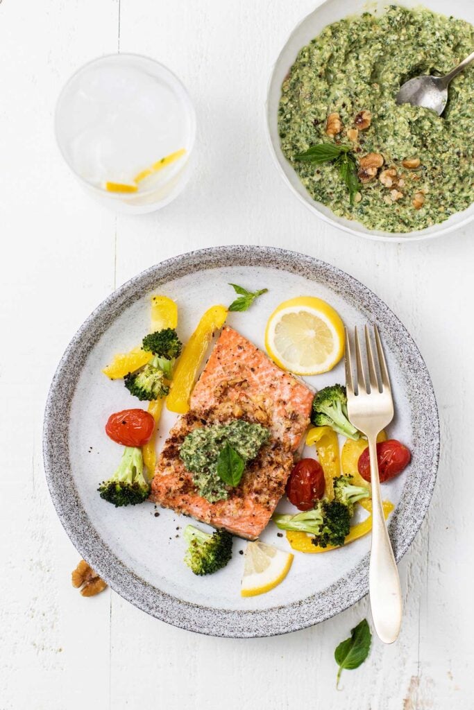 A plate with salmon and pesto served with veggies, next to a bowl of vibrant green pesto.