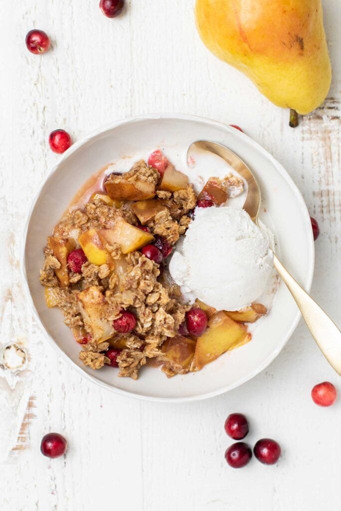 A bowl with a serving of pear crisp with cranberries and vanilla ice cream.