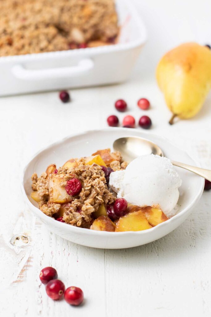 A bowl of pear crisp served with ice cream in front of a baking dish.
