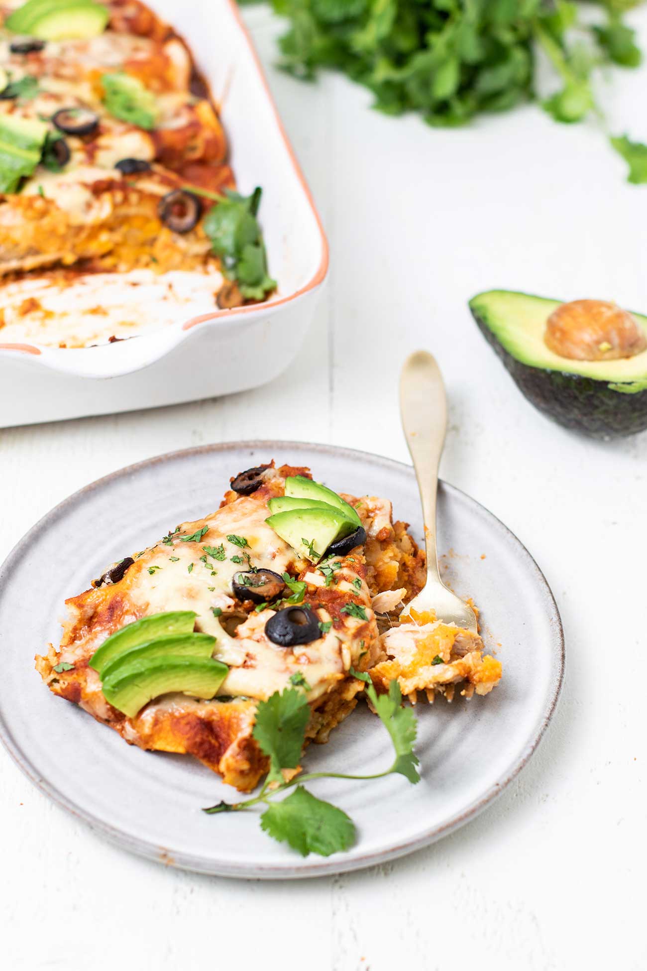 A plate with turkey enchiladas garnished with avocado and cilantro.