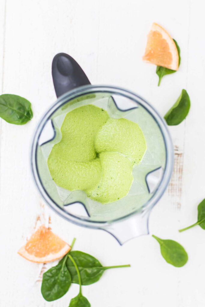 A bright green smoothie shown with a thick texture in a blender.