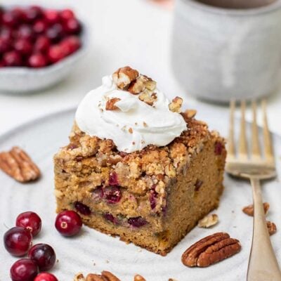 A slice of pumpkin cranberry coffee cake topped with whipped cream.
