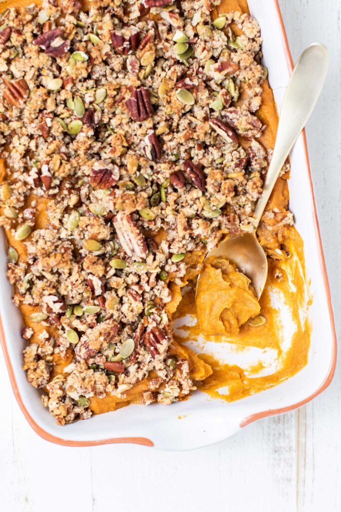 A close up look at a healthy sweet potato casserole with a spoon taking a serving.