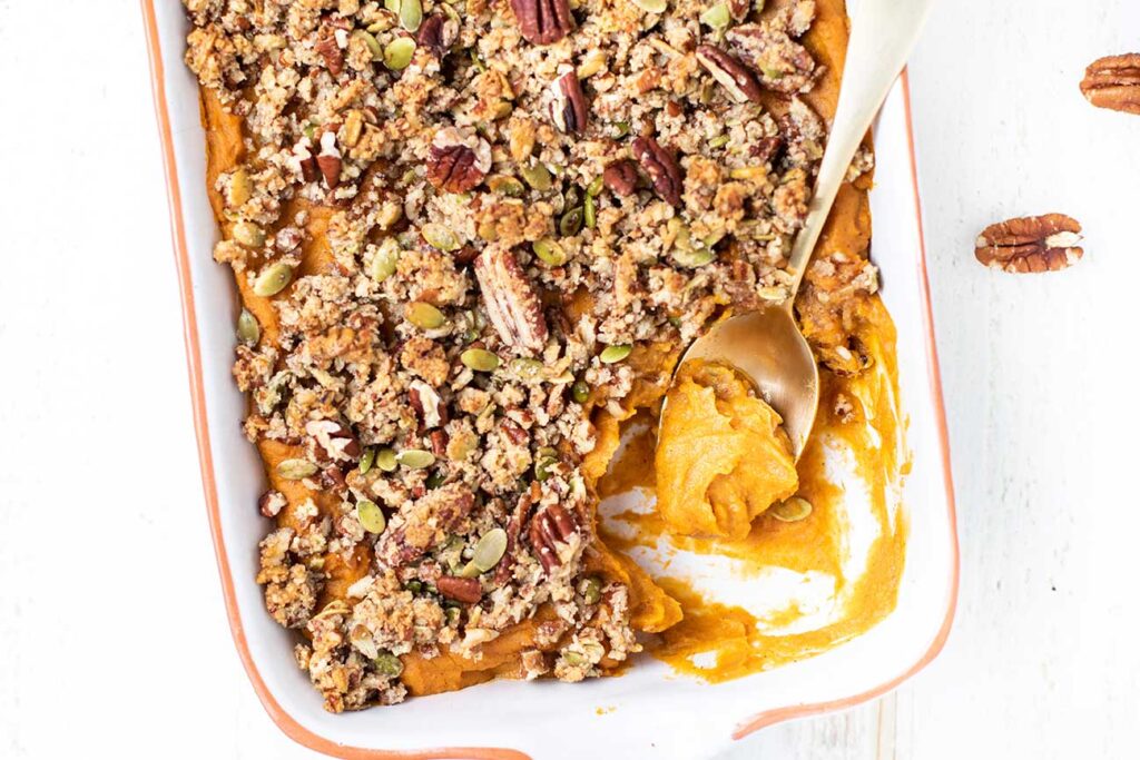 A close up look at a healthy sweet potato casserole with a pecan crumble topping in a baking dish.
