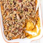 A close up look at a healthy sweet potato casserole with a pecan crumble topping in a baking dish.