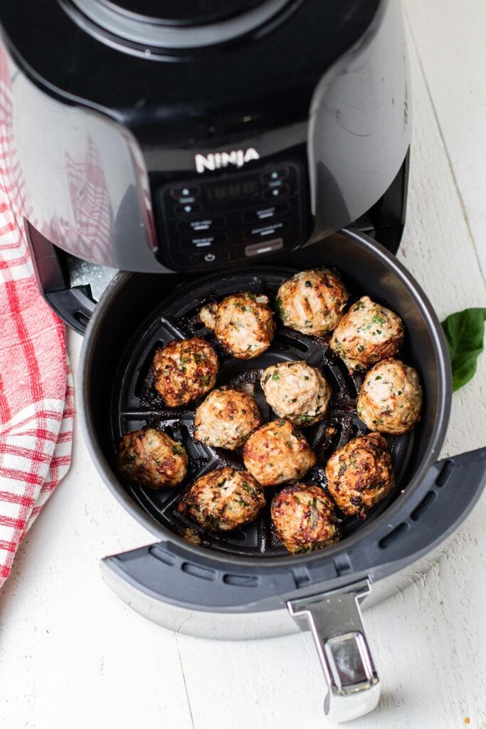 An air fryer with turkey meatballs shown cooked.