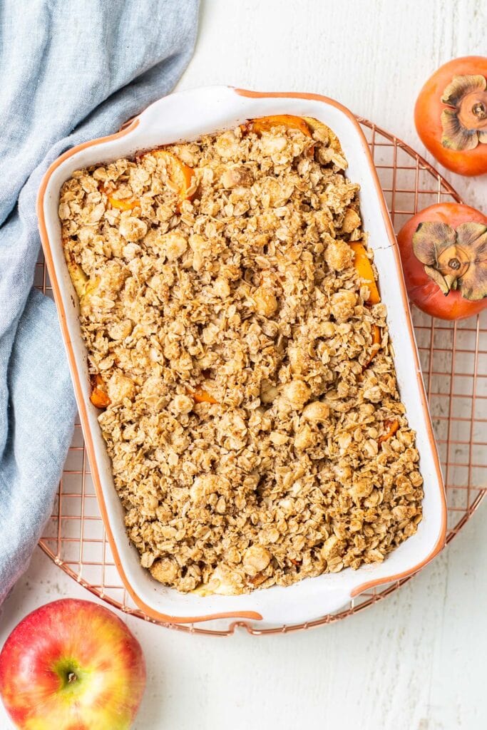 A baking dish of persimmon apple crisp shown on a cooling rack.